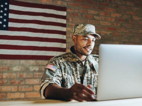 Person in military clothing sitting in front of a laptop.
