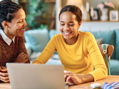 A mom and teen daughter looking at a laptop.