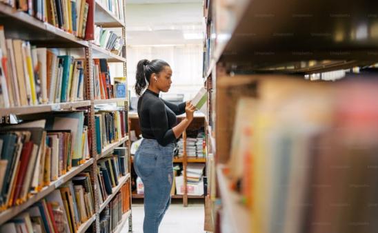 A young woman looks at a shelf of books in a library.