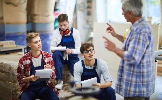 Adult male speaking to three college aged males in a workshop.