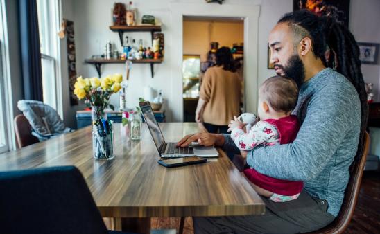 Father sitting at a computer holding a young child.