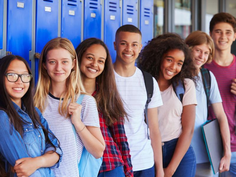 Seven high school students along a set of blue lockers, smiling at the camera.