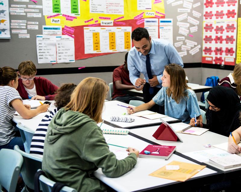 A high school classroom with a teacher helping students at their desk. 