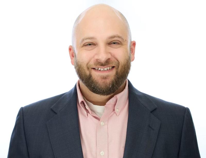 Headshot of Josiah wearing a pink button up shirt with a grey suit coat.