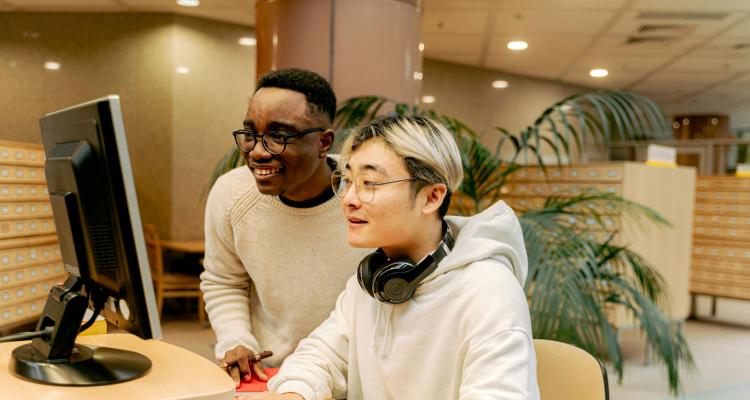 A person helping someone use a computer in a library